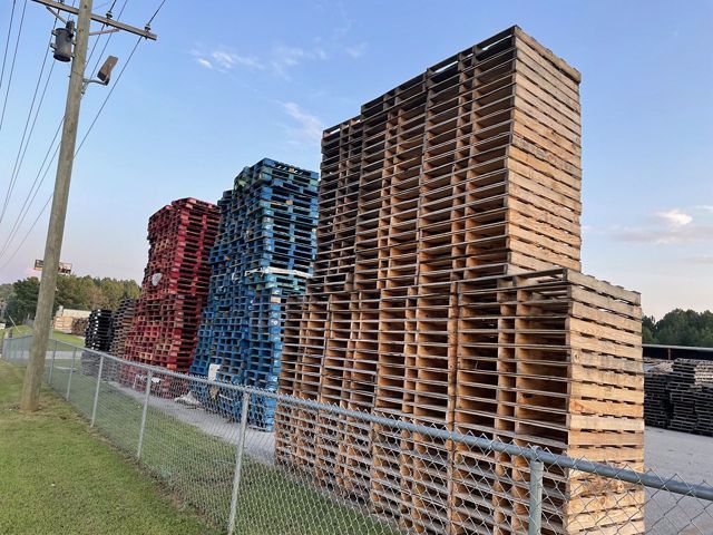 a stack of wooden pallets behind a chain link fence.